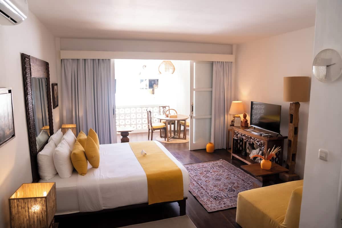Een hotelkamer met een bed, een televisie, een bureau en een balkon met een tafel en stoelen.