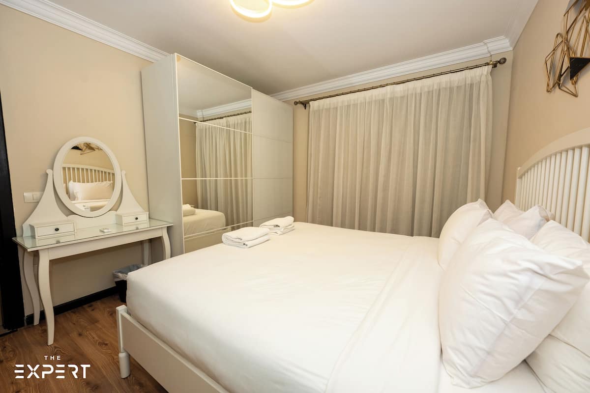 A hotel room with a large bed, a vanity with a mirror, and a wardrobe.