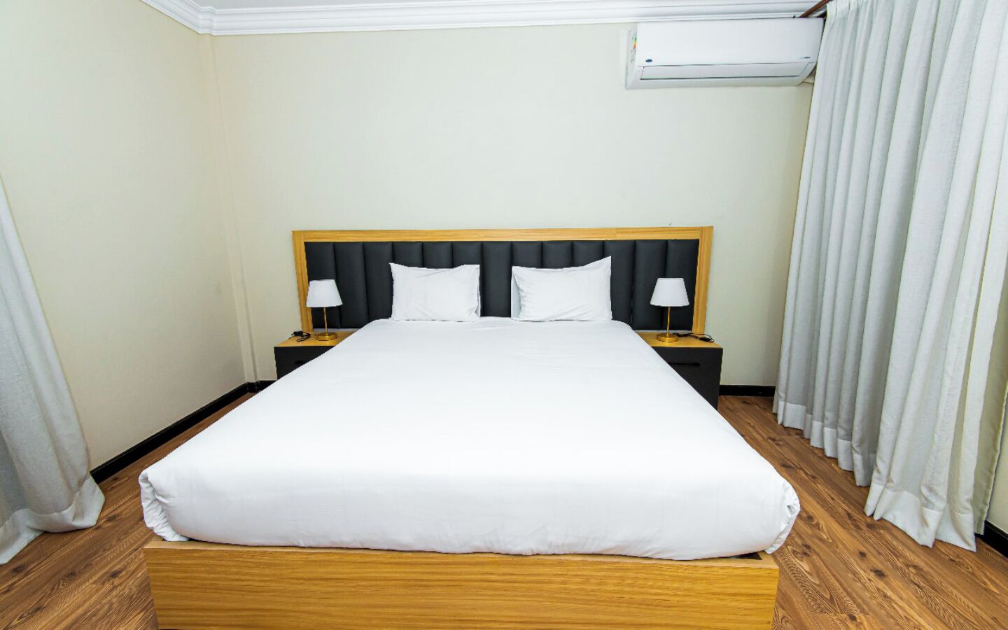 A hotel room with a large bed, two bedside tables with lamps, and a window with curtains.