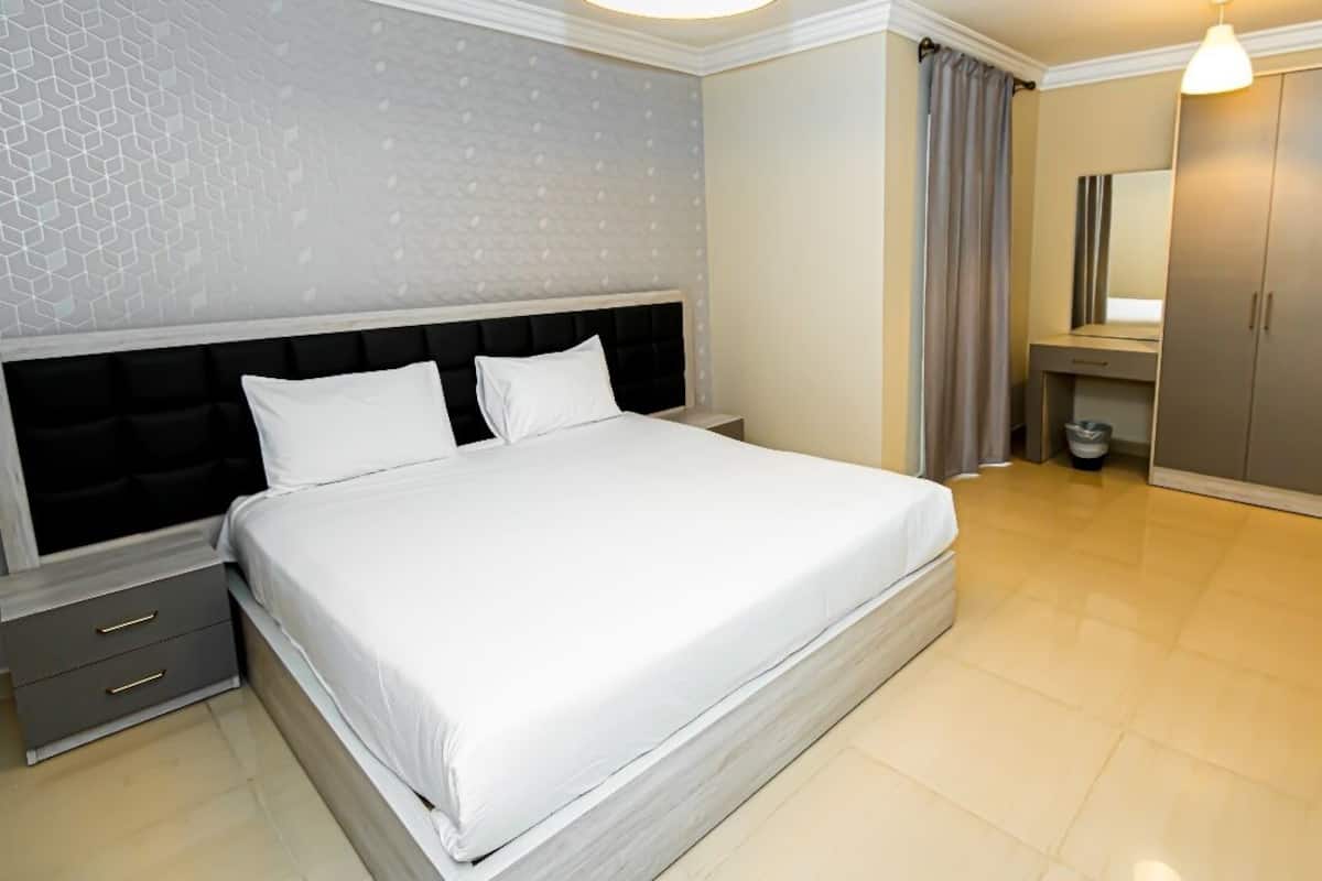 A modern bedroom with a large bed, a nightstand, a wardrobe, and a bathroom with a mirror and curtains.