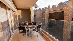 A balcony with a table and chairs, a glass railing, and a view of a building with stone pillars. - The Expert (Cairo)