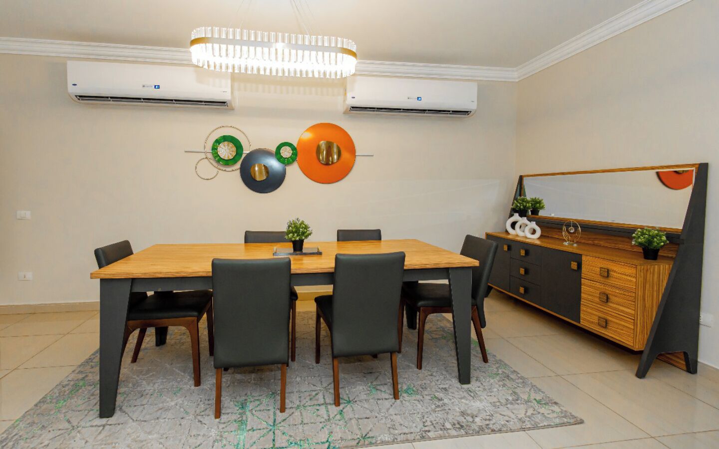 Een eetgedeelte met een houten tafel, zwarte stoelen, een kroonluchter en een decoratief wandobject.
