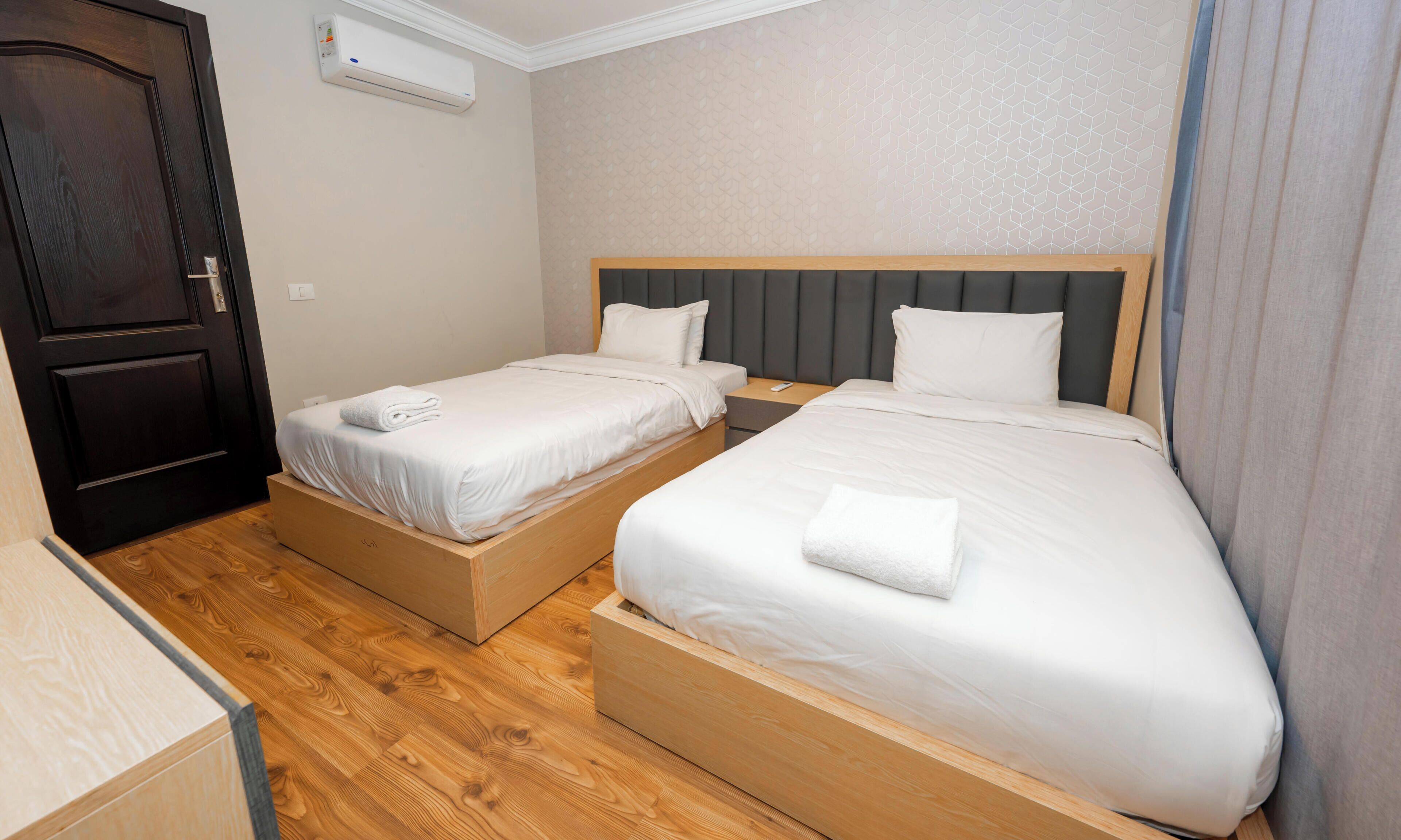 Een hotelkamer met twee eenpersoonsbedden, een houten vloer, een donkere deur en een witte airconditioning.