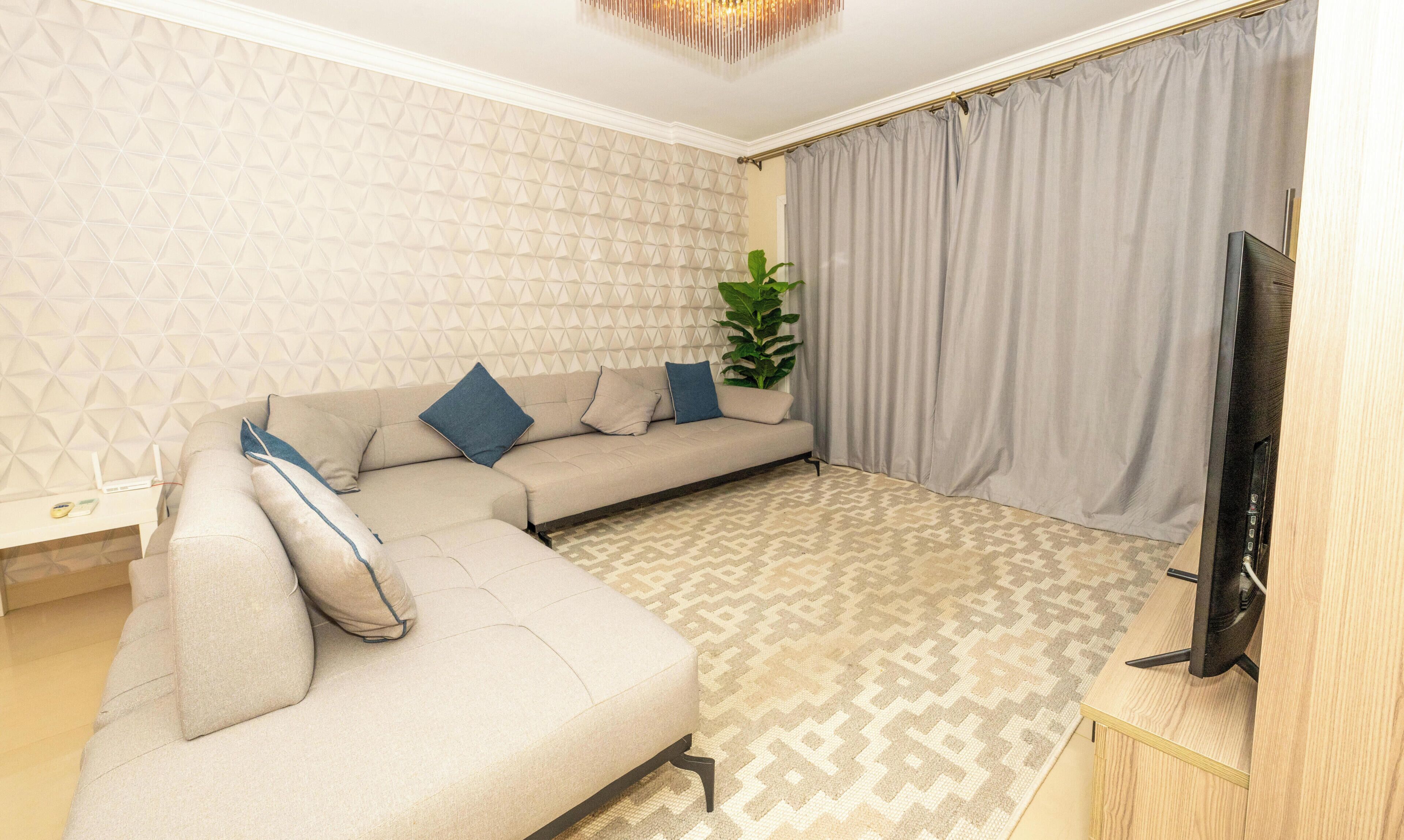 A modern living room with a sectional sofa, a flat-screen TV, and a patterned rug.