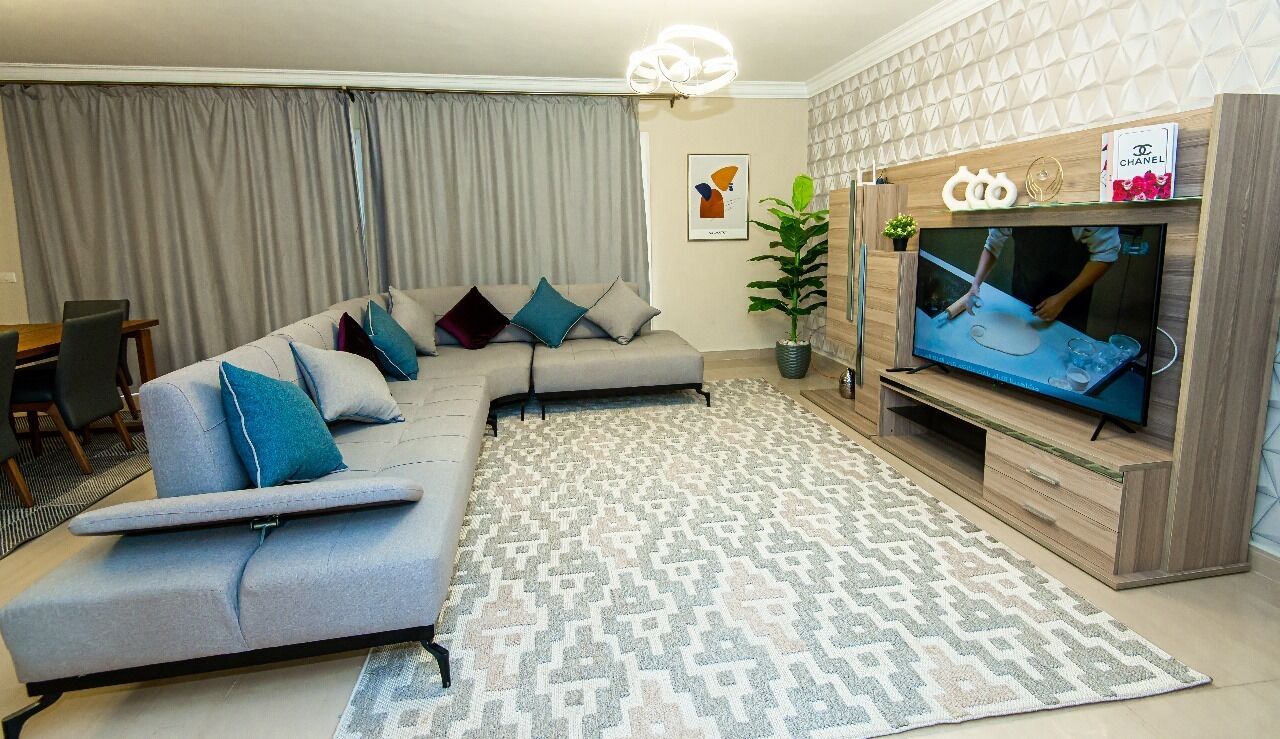 A modern living room with a sectional sofa, a flat-screen TV, and a patterned rug.