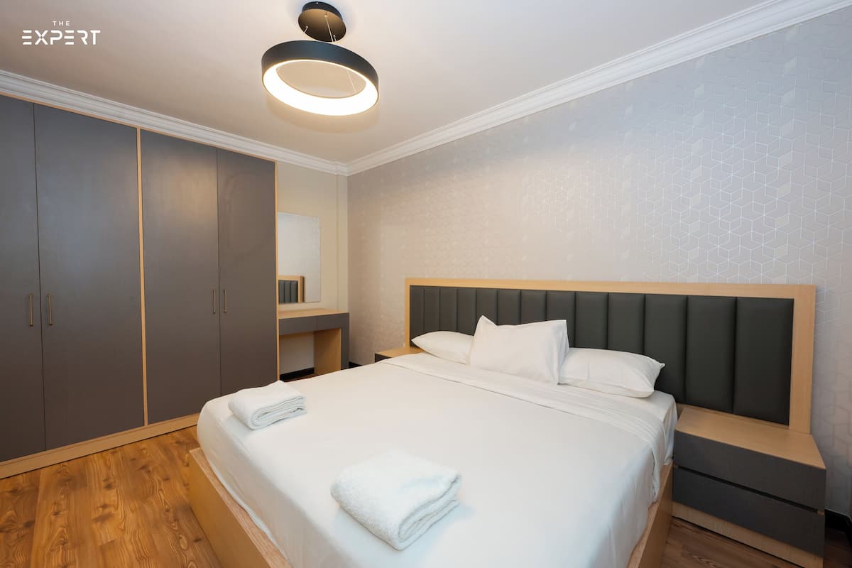A modern hotel room with a large bed, a wardrobe, and a vanity area.