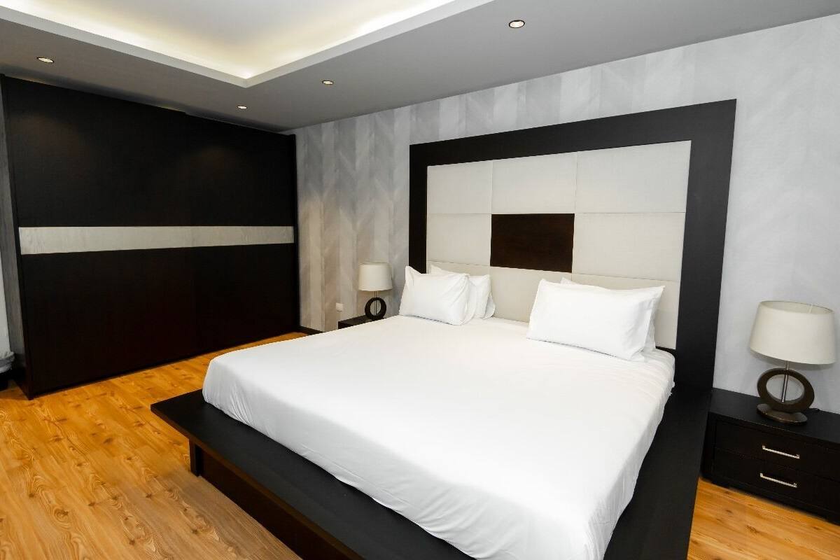 A modern bedroom with a large bed, dark wood flooring, and a minimalist design.