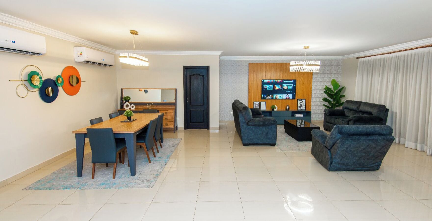 A modern living room with a dining area, featuring a sofa set, a coffee table, and a TV mounted on the wall.