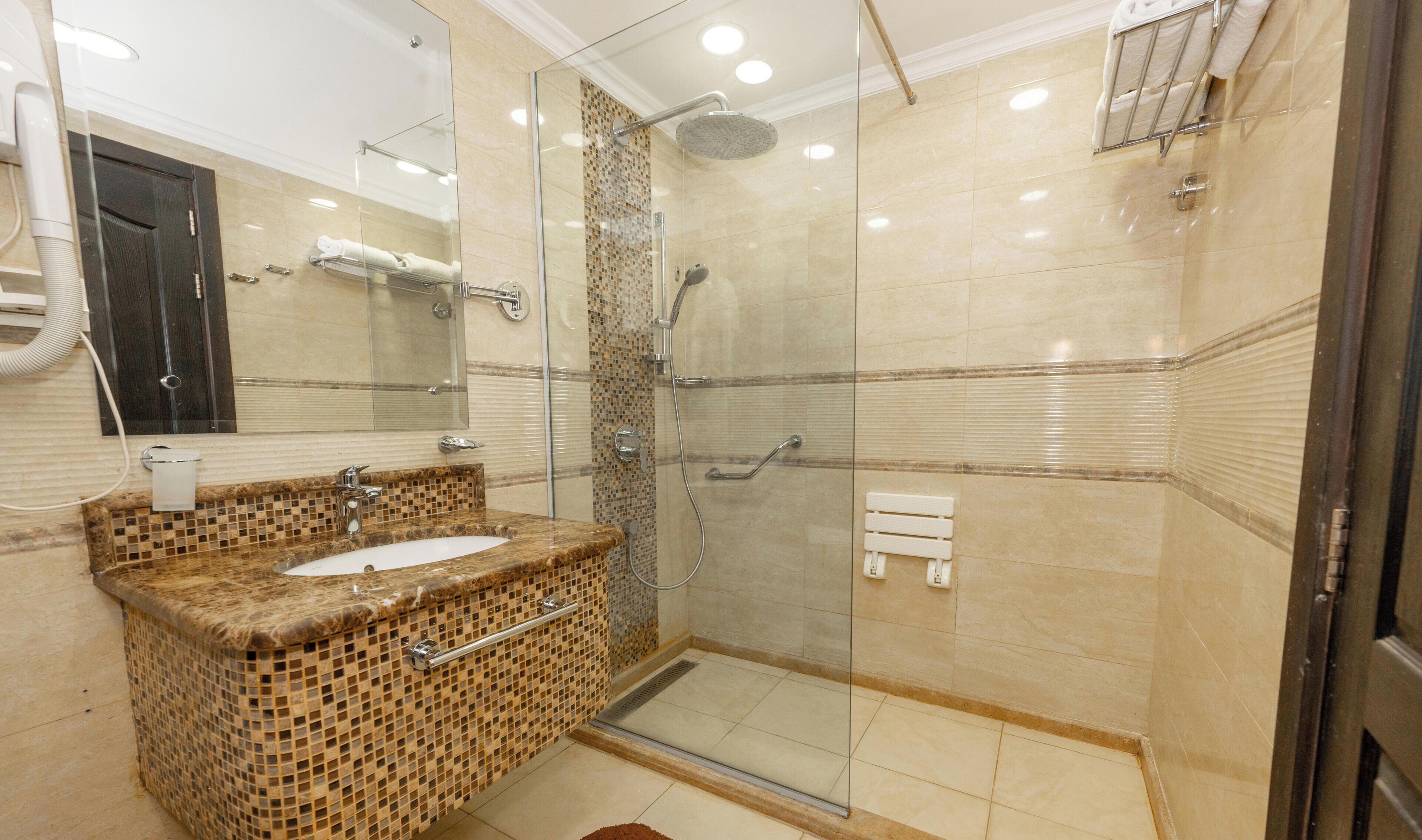 A modern bathroom with a glass-enclosed shower, a sink with a mosaic countertop, and a mirror above the sink.