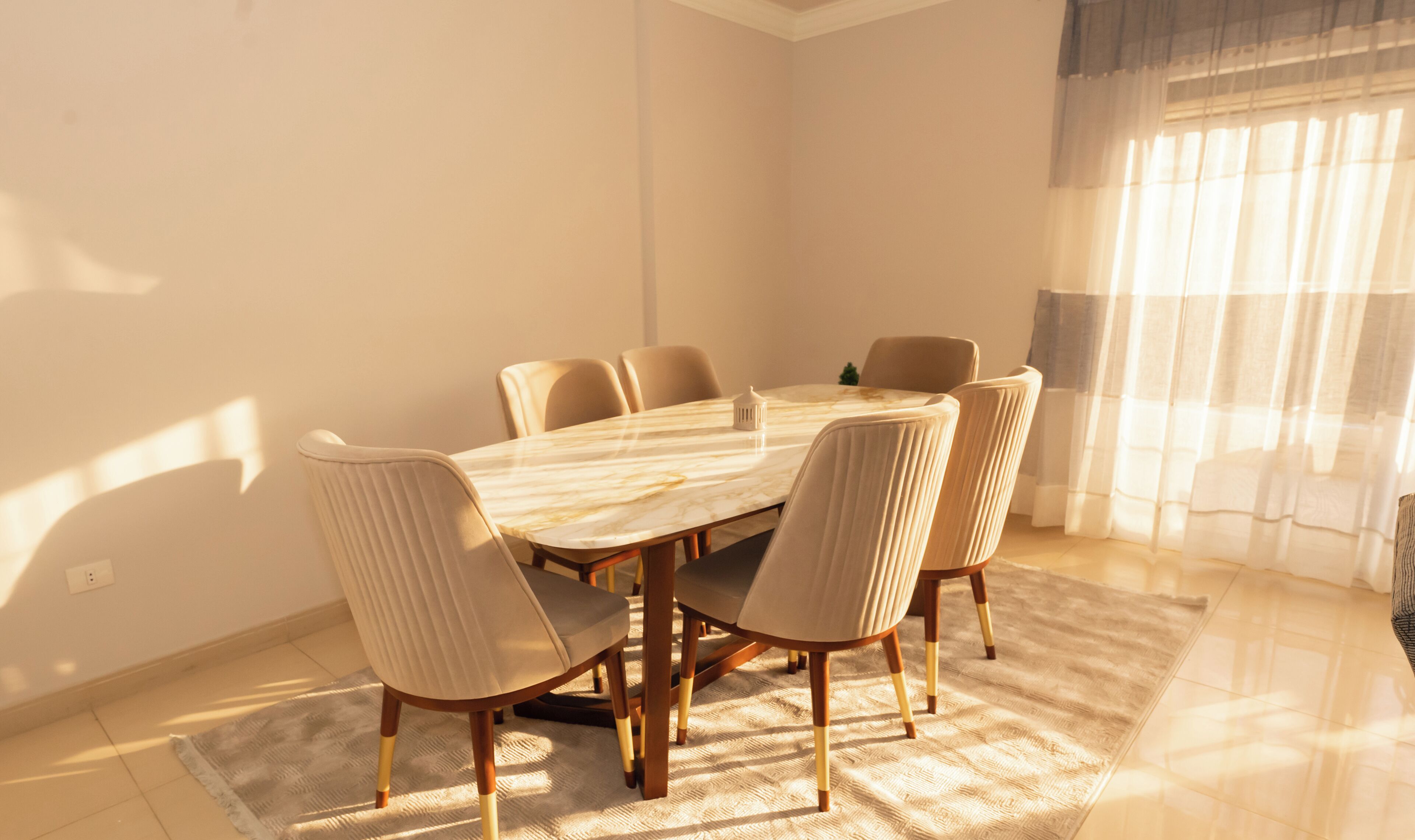 A dining area with a marble table, six upholstered chairs, and a rug.