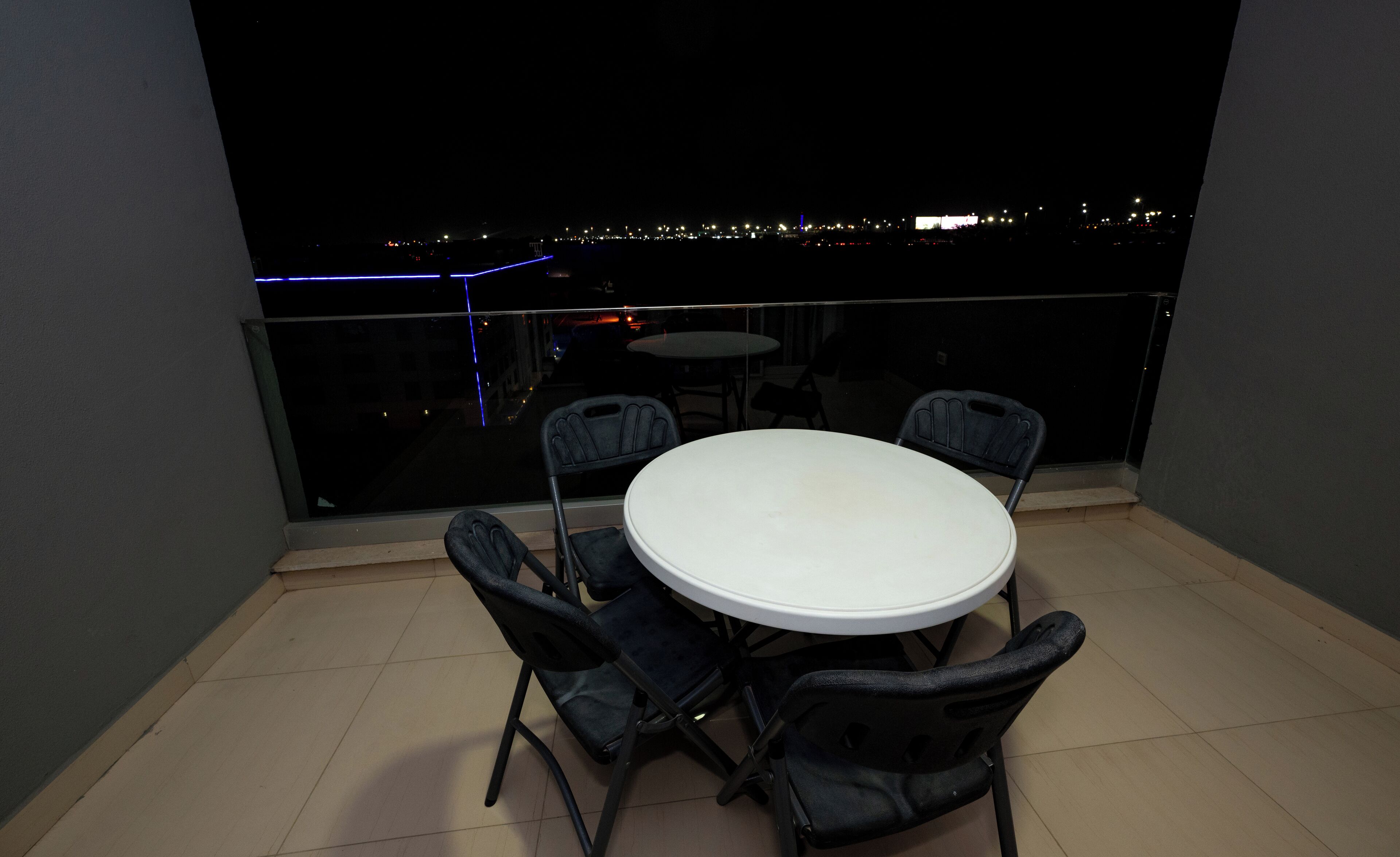 Een balkon met een ronde tafel en vier stoelen, met uitzicht op een stadsgezicht in de nacht.