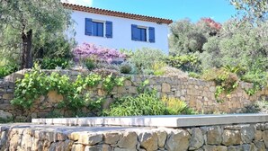 A white building with blue shutters, surrounded by stone walls and various plants. - Peaceful farmhouse surrounded by olive trees.  Only 15 minutes from beaches and mountains (Opio)