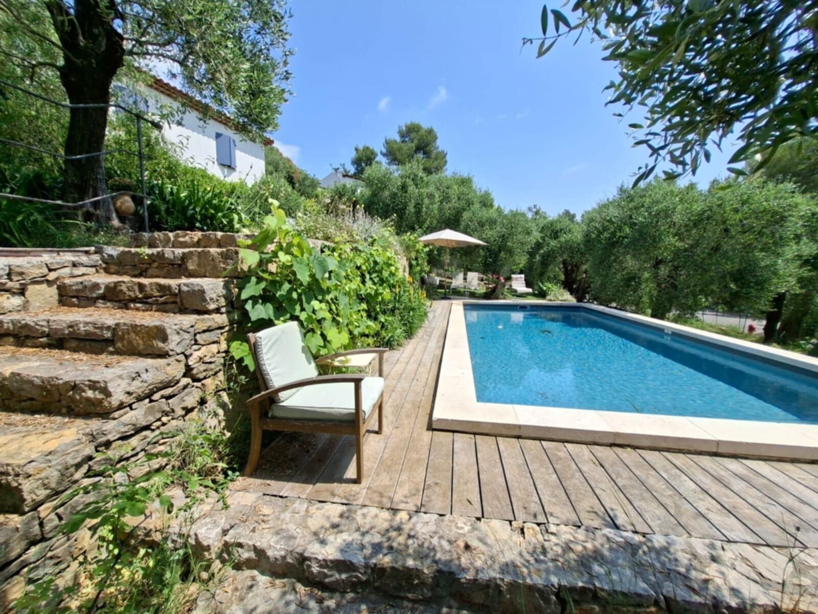 Una piscina amb un gratell de fusta, una paret de pedra i una cadira.