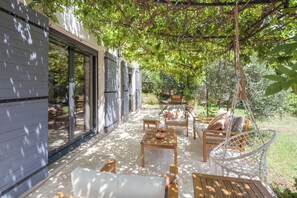 A covered patio area with outdoor furniture, a swing, and a view of the surrounding garden. - Peaceful farmhouse surrounded by olive trees.  Only 15 minutes from beaches and mountains (Opio)