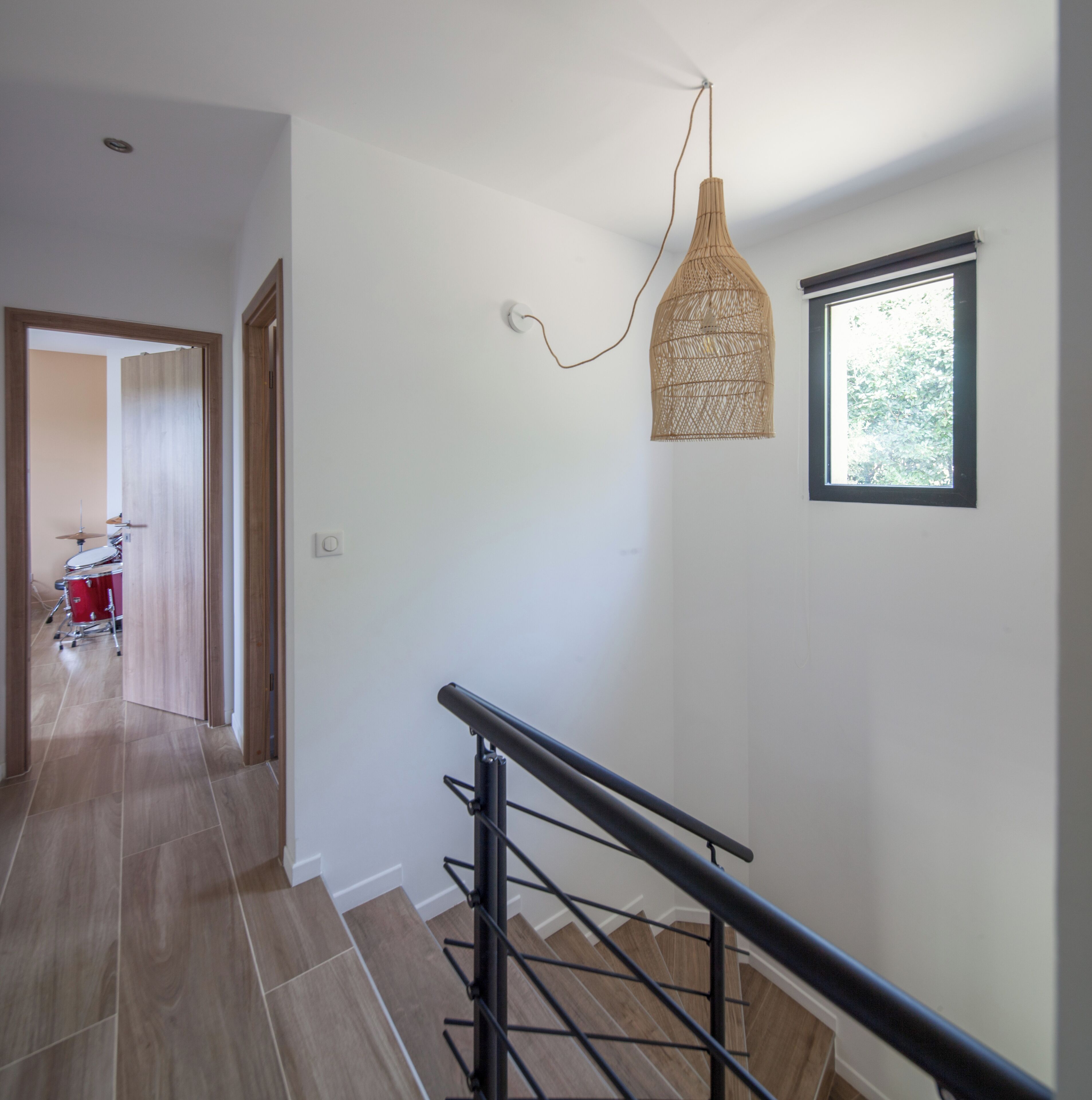 A modern interior with a staircase, a hanging light fixture, and a window with a view of greenery.