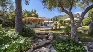 A landscaped garden with a pool, stone steps, and a house with a tiled roof. - My Rental Homes - Can Cabana with private pool, air conditioning and wifi (Pollença)
