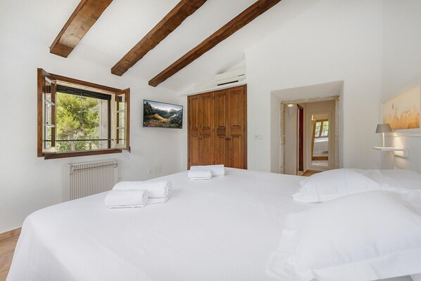 Une chambre avec un grand lit, des poutres apparentes, une fenêtre donnant sur un beau paysage, un radiateur et une porte menant à une autre pièce.