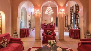 A luxurious hotel lobby with red velvet sofas, a central dining area, and ornate chandeliers. - My Rental Homes - Dar Maril with pool, tennis court and garden (Oulad Jellal)
