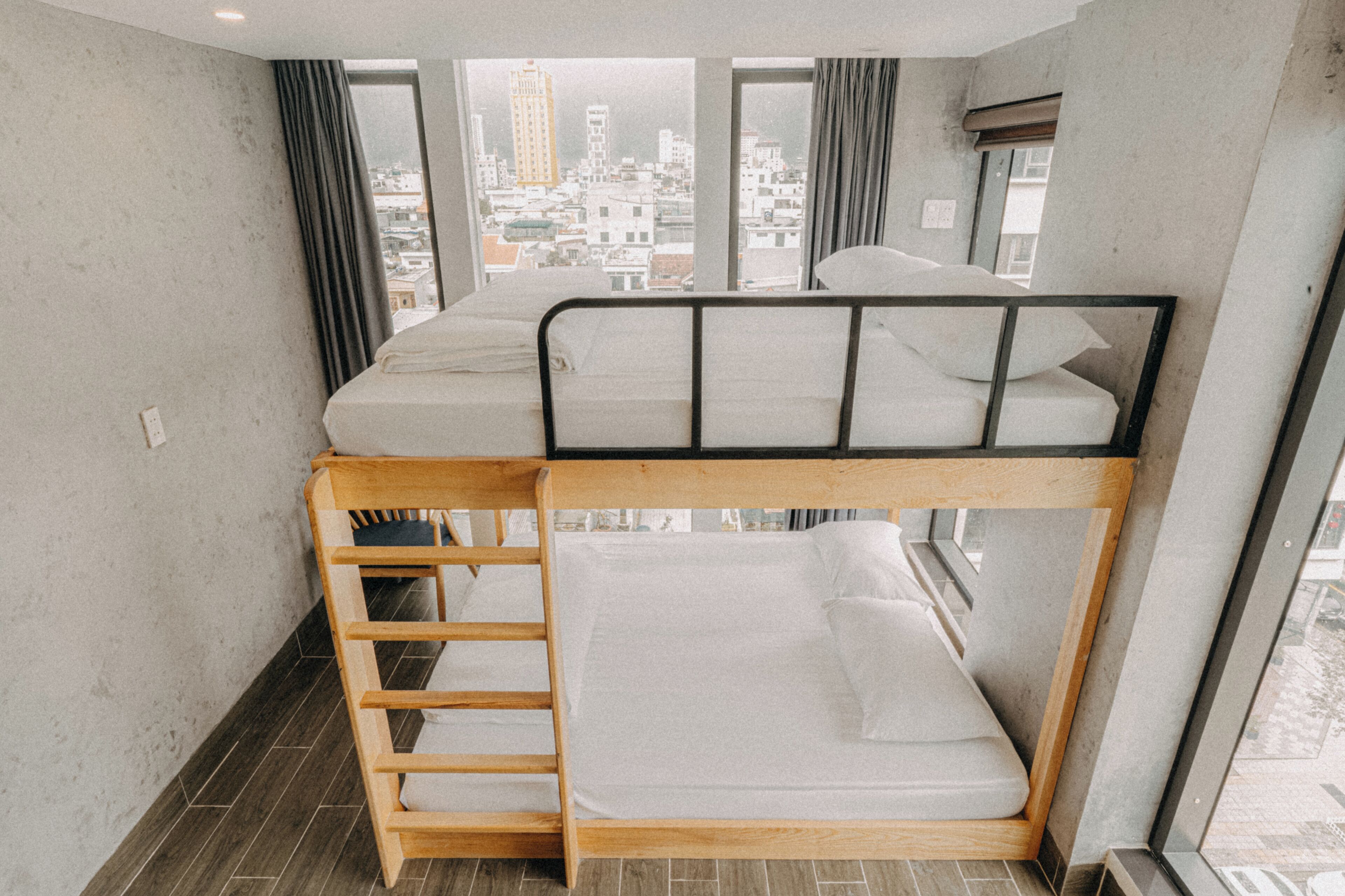 A bunk bed room with a city view, a window with curtains, and a wooden ladder.