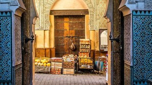 Un arc ornamentat amb treball de rajola detallat, que condueix a una zona de mercat amb parades de fruita i una porta de fusta.