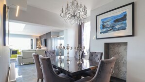 A modern dining room with a glass table, upholstered chairs, a chandelier, and a framed painting on the wall. - Bronallt (Cemaes Bay)
