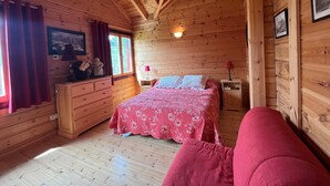 Een slaapkamer in een houten blokhut, met een bed, een dressoir en een raam met gordijnen.