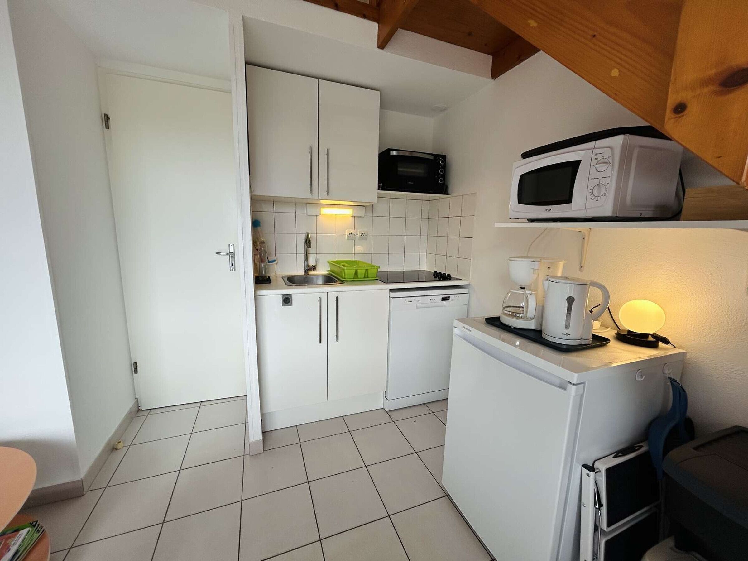 Una cocina compacta con armarios blancos, un microondas, una cafetera y un refrigerador pequeño.
