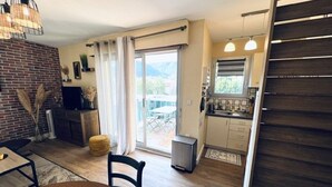 A compact living space with a dining area, kitchenette, and a sliding glass door leading to a balcony.