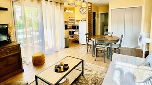 A living room with a sofa, a coffee table, and a TV. There is a dining area with a table and chairs. The room has a large window with curtains.