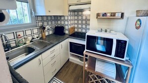 A compact kitchen with a sink, microwave, and a clock on the wall.