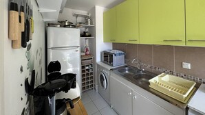A compact kitchen with a white refrigerator, a washing machine, a microwave, and green cabinets.