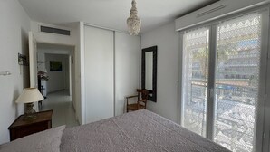 A bedroom with a bed, a chandelier, a mirror, and a window with patterned curtains.