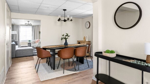 Ett modernt matområde med ett runt bord, fyra stolar, en vas med blommor, en klocka och en spegel på väggen.