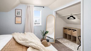 Ett sovrum med en säng, en stor spegel, en krukväxt, en hängande lampa och en garderob med hyllor.