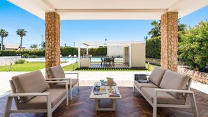 A covered outdoor seating area with two sofas and a coffee table, overlooking a pool and garden. - Villa Agorà with private pool - My Rental Homes (Syracuse)