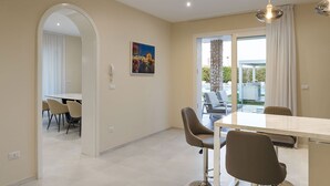 A modern dining area with a large table and chairs, a painting on the wall, and a view of the outdoor patio. - Villa Agorà with private pool - My Rental Homes (Syracuse)