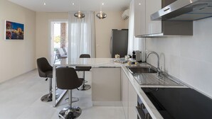 A modern kitchen with a central island, bar stools, a built-in oven, and a stainless steel range hood. - Villa Agorà with private pool - My Rental Homes (Syracuse)