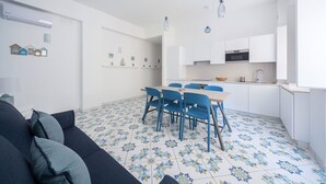 Een compacte leefruimte met een eethoek, een kitchenette en een bank met kussens.