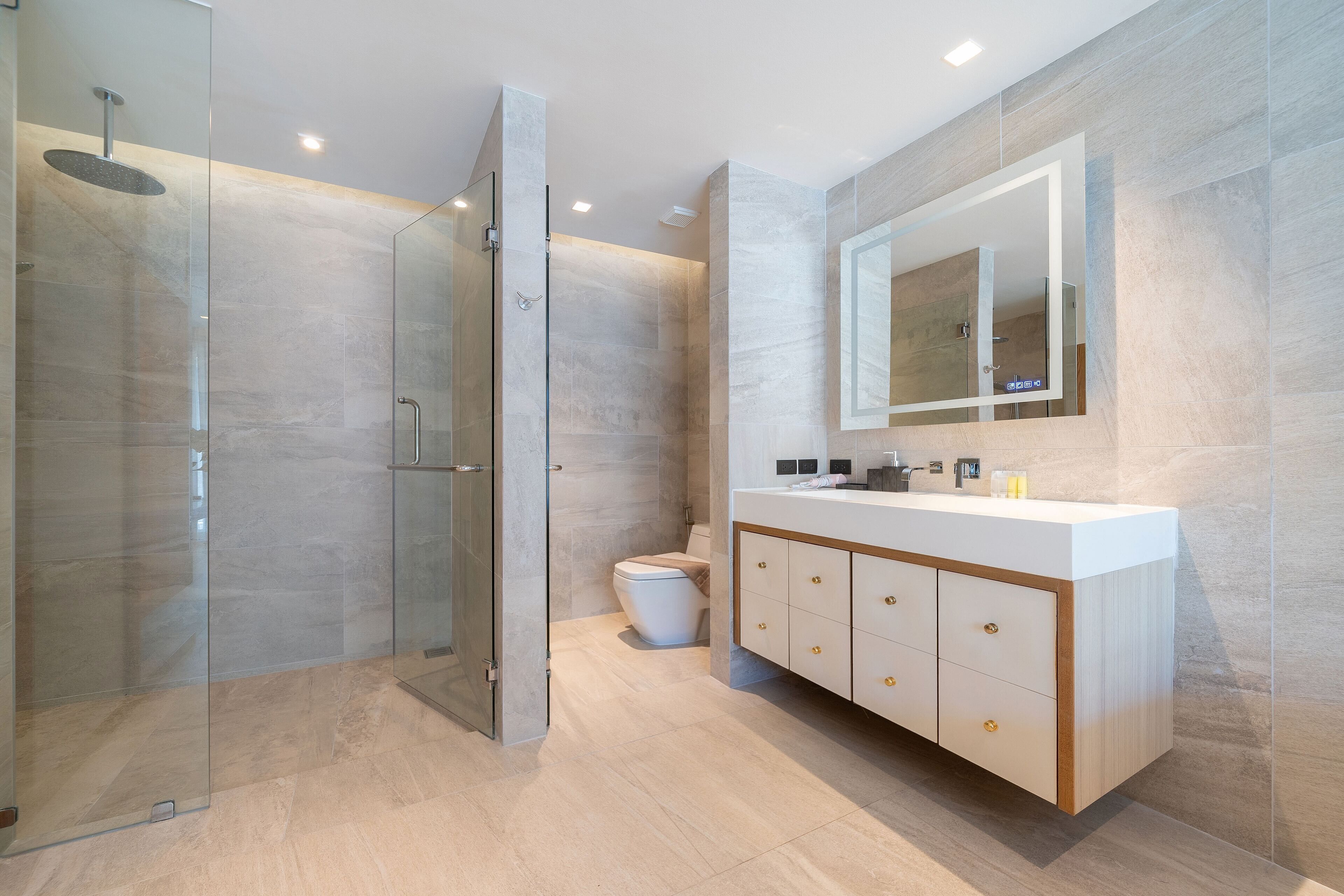 A modern bathroom with a glass-enclosed shower, a white toilet, and a vanity with a mirror and cabinet.