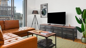 A modern living room with a leather sofa, a flat-screen TV, a lamp, and a large potted plant. - Central Charming 2 Bedrooms With Balcony Aircon (Sydney)