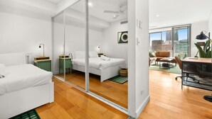 A modern hotel room with a glass partition, a bed, a desk, and a view of the city. - Central Charming 2 Bedrooms With Balcony Aircon (Sydney)