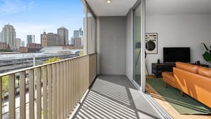 A modern apartment with a balcony overlooking a cityscape, a living area with a sofa and a flat-screen TV, and a framed poster on the wall. - Central Charming 2 Bedrooms With Balcony Aircon (Sydney)