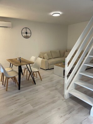 Una sala de estar moderna con una mesa de comedor de madera, sillas blancas, un sofá beige y una escalera blanca.