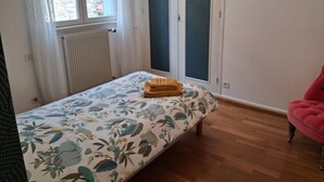 A bedroom with a bed, a window, a radiator, and a pink chair. - Gîte "Chez Tété (Meursault)