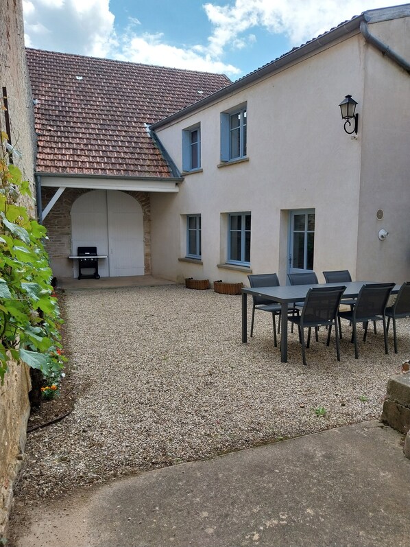 A building with a tiled roof, a covered patio area with a grill, and a table with chairs. - Gîte "Chez Tété (Meursault)