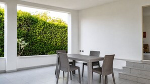 Un espace repas moderne avec une table et des chaises, une vue sur la verdure et un escalier menant à un niveau supérieur.