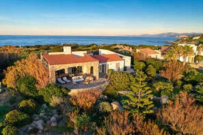 Una casa costera con un patio de piedra, mobiliario exterior y vista al mar.