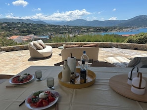 Una terraza con mesas al aire libre, una mesa de comedor con platos de comida, una botella de agua y vasos.