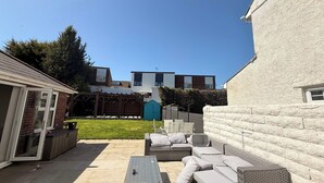 Un jardin avec un espace patio, du mobilier d’extérieur, un petit abri de jardin et une maison à la façade en briques et à l’extérieur blanc.