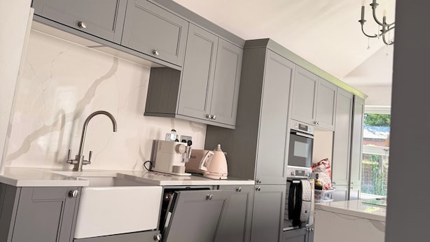 Une cuisine moderne avec des meubles gris, un plan de travail blanc, un four encastré et une machine à café.